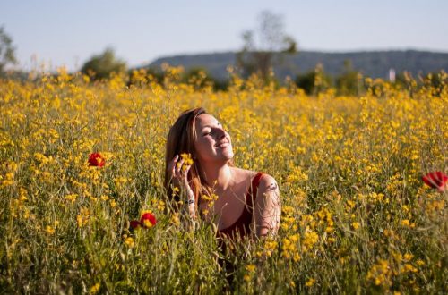 A woman sits with eyes closed, enjoying the sun in a vibrant yellow flower field.