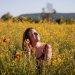 A woman sits with eyes closed, enjoying the sun in a vibrant yellow flower field.